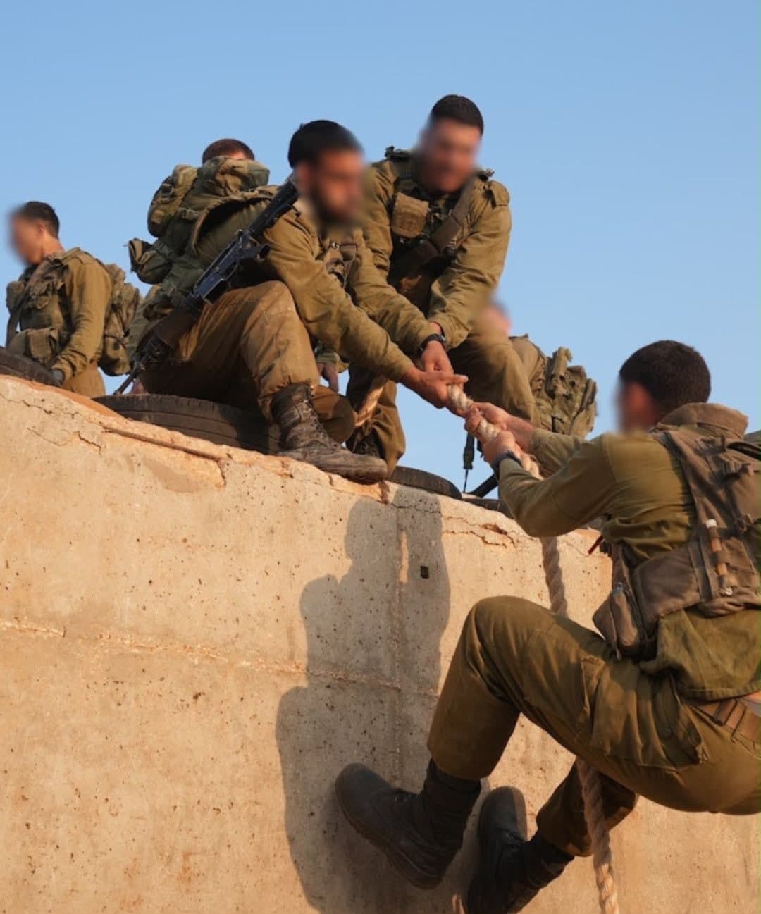 לוחמים על קיר בטון מושיטים יד וחבל ללוחם שמטפס אליהם במסלול המכשולים