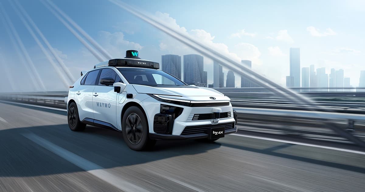 רכב שטח חשמלי לבן של טויוטה, דגם bZ4X, עם הכיתוב WAYMO וחיישנים על הגג, נוסע על גשר מול קו רקיע של עיר